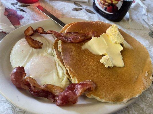 Two large and fluffy pancakes topped with butter. 2 eggs. 2 strips of bacon.