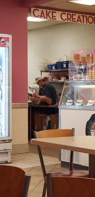 Employee sitting with shoes and butt on table where "cake creations" and other food products are made and served. Absolutely disgusting.