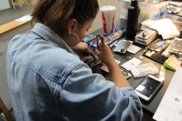 Technician disassembling an iPhone's components in preparation for moving the logic board into a new frame