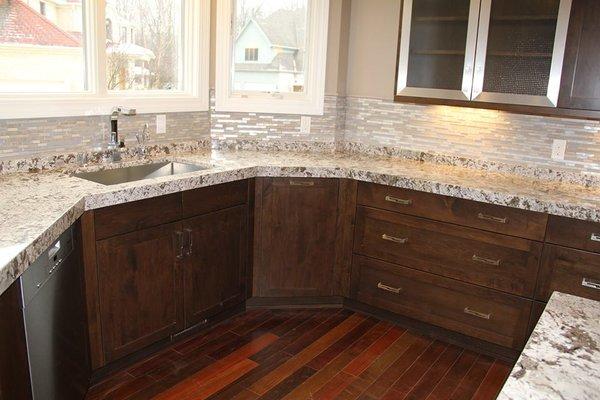 Kitchen cornering granite and sink with stone backsplash.