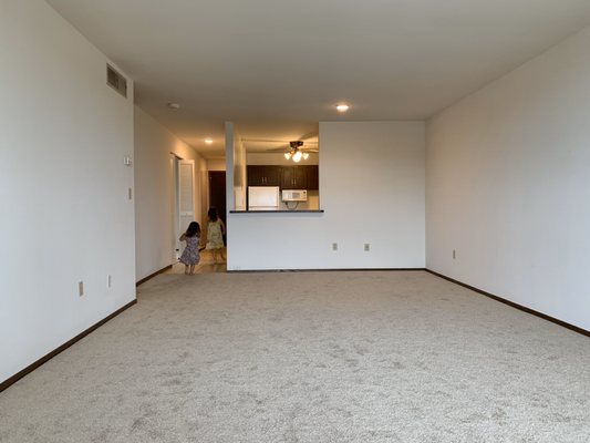 Living room space with a window opening overlooking into the kitchen with a den room on the left side in the hallway.