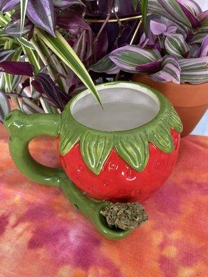 A pipe that is also a coffee cup in the shape of a strawberry with a cannabis nug in the bowl.