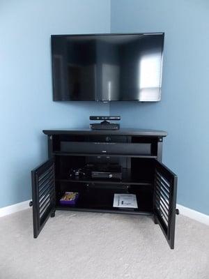 42" TV mounted in a special corner mount with a Polk Audio soundbar and subwoofer that is hidden behind the cabinet.