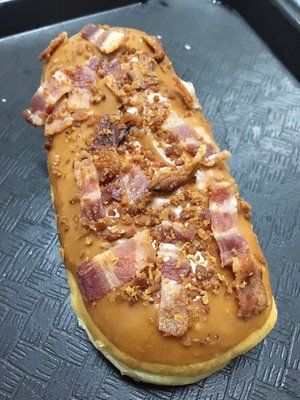 Maple covered donut with bacon bits sprinkled on top.