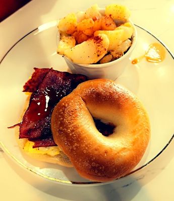 Bacon egg and cheese on a plain bagel with a side of home fries.