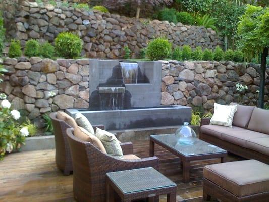 board-form concrete water feature creates lovely atmosphere for outdoor living room and makes use of steep sloped garden