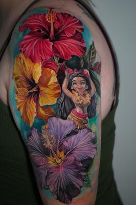 Wrapped in vivid hibiscus, this tattoo of a hula girl nods to classic car culture, blending vibrant tradition with a touch of nostalgia.