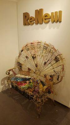 "ReNew" exhibit. "Garden Bench" by Monica Cioppettini. Renewed with beaded necklaces, costume jewelry and faux eyelashes.