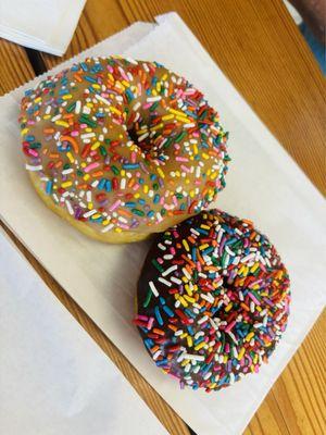 a vegan  raised, maple-glazed, rainbow sprinkle donut + a vegan  chocolate cake, chocolate glazed, rainbow sprinkle donut