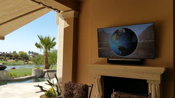 Samsung 65" LED TV w/ Sonos Play Bar mounted outdoor on patio over fireplace.