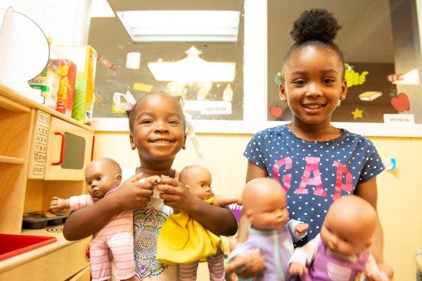 Two girls playing with dolls during play time.