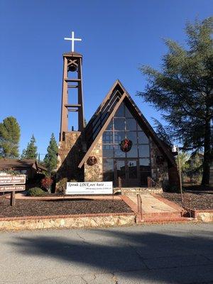 Front entrance to sanctuary with tall pitched roof, bell tower and banner "speak Love not hate"