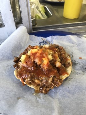 This is a pastor with cheese on a crunchy tortilla topped with pineapple pico de gallo and red pastor sauce.