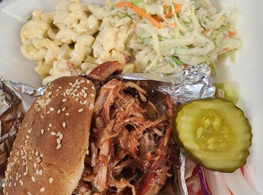 Pulled pork sandwich paired with cole-slaw and macaroni salad. Pickles and grilled onions are a great topper for this sandwich!