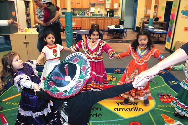 Children in traditional Mexican costumes dancing to Spanish music.