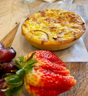 Homemade Quiche Featured specialty cheese, an abundance of meat, roasted vegetables, fresh herbs, and seasonings, served with fruits.