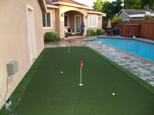 Putting green with chipping area, fringe finish & three holes next to the pool in a backyard  in San Jose, California.