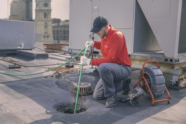 Technician power jetting stack lines from the roof of a commercial building. Stack, Snake, Roof, Drains