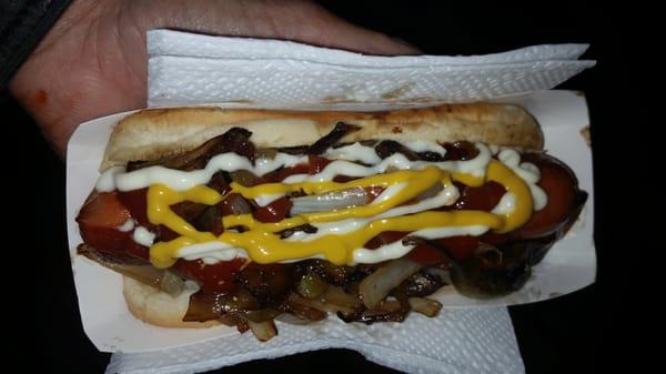 Bacon wrapped dog with the works, grilled onions, peppers, mustard, mayo, ketchup and roasted chilli on a warm bun.