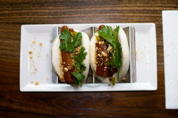 Taiwanese Pork Belly Bao Braised pork belly served with steamed bao bun, pickled mustard green, powdered peanuts with sugar, and cilantro.