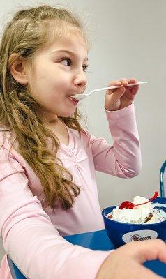 Scoops and spoons young girl eating ice cream sundae