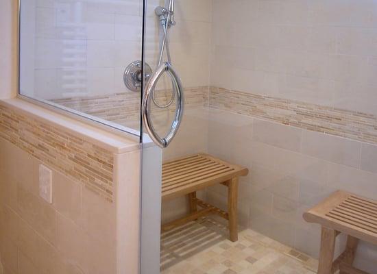 Shower-steam room with teak benches. Walls are Bulgarian limestone with gold accent limestone rail mosaic. Handshower is tempera