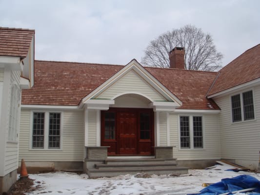 Front of the house with mahogany door with wood clapboard on the walls and wood shakes on the roof