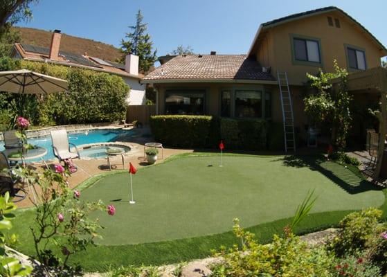 Putting green with fringe finish and four holes between the patio and the pool in a backyard in San Jose, California.