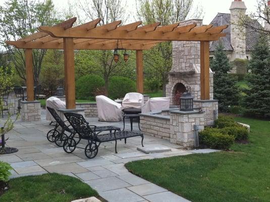 Natural stone fireplace, walls and bluestone patio with cedar pergolla creates this outdoor room